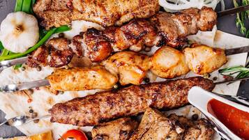 Variedad de carnes a la parrilla, incluyendo brochetas y costillas, servidas en una tabla de pizarra con guarniciones como cebollas y hierbas aromáticas.