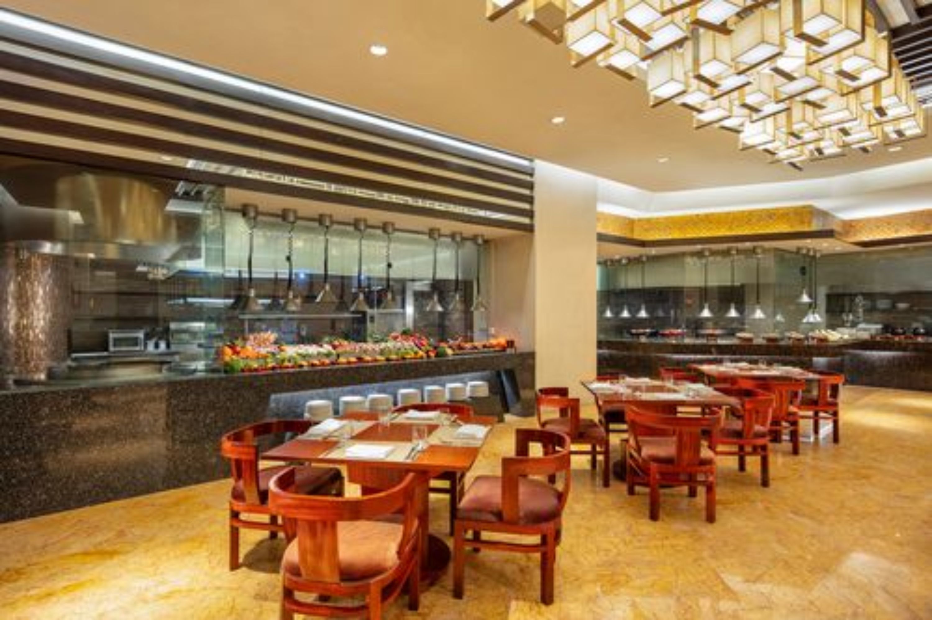 A restaurant with a buffet setup, wooden tables and chairs, and a modern interior design.