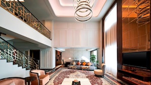 A spacious living area with a large sofa, coffee table, and a flat-screen TV. A staircase with a decorative railing leads to an upper level. - Sheraton Xi'an North City Hotel (Xi'an)