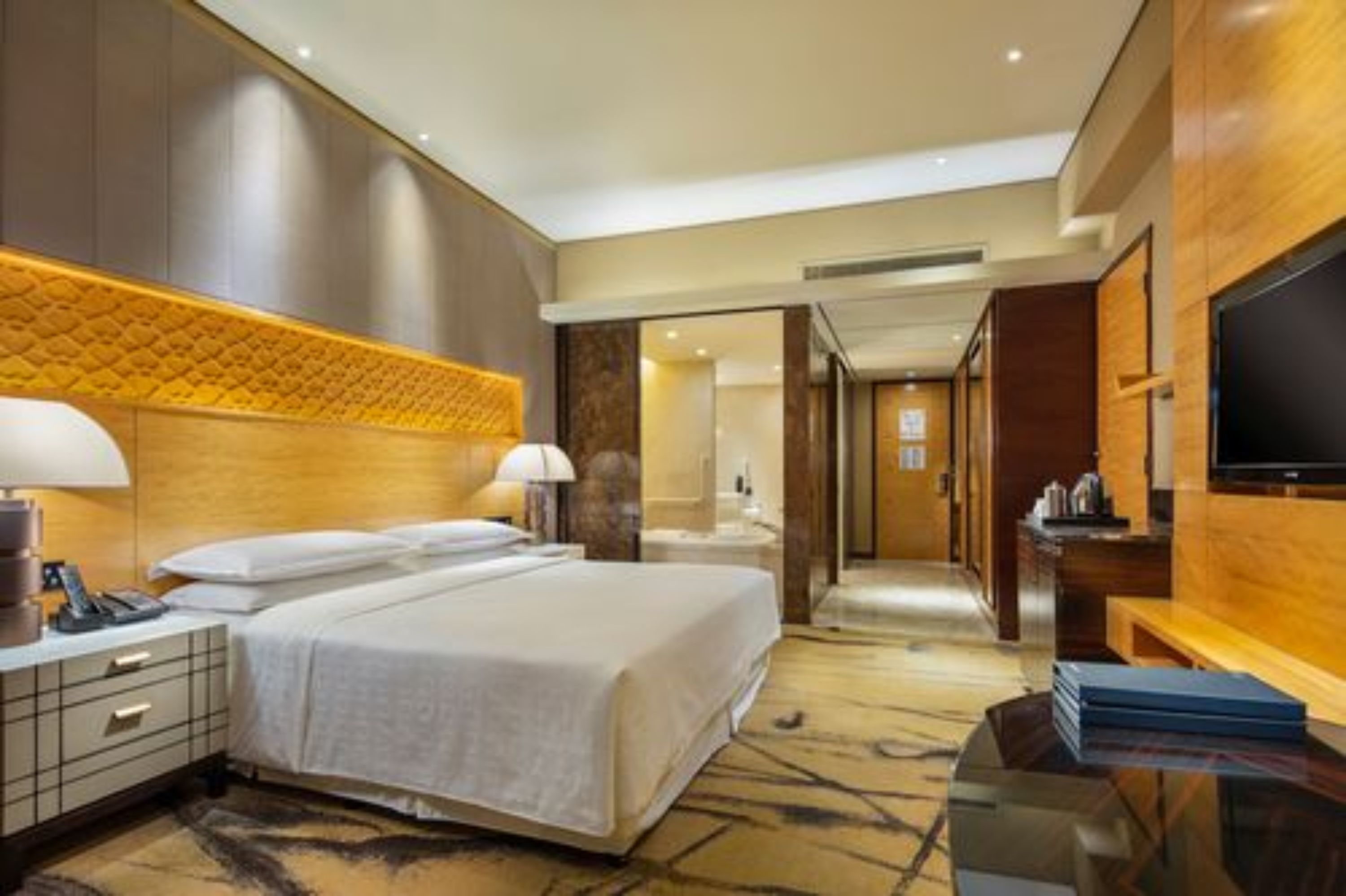 A hotel room with a large bed, bedside tables, a flat-screen TV, and a bathroom visible through an open door.