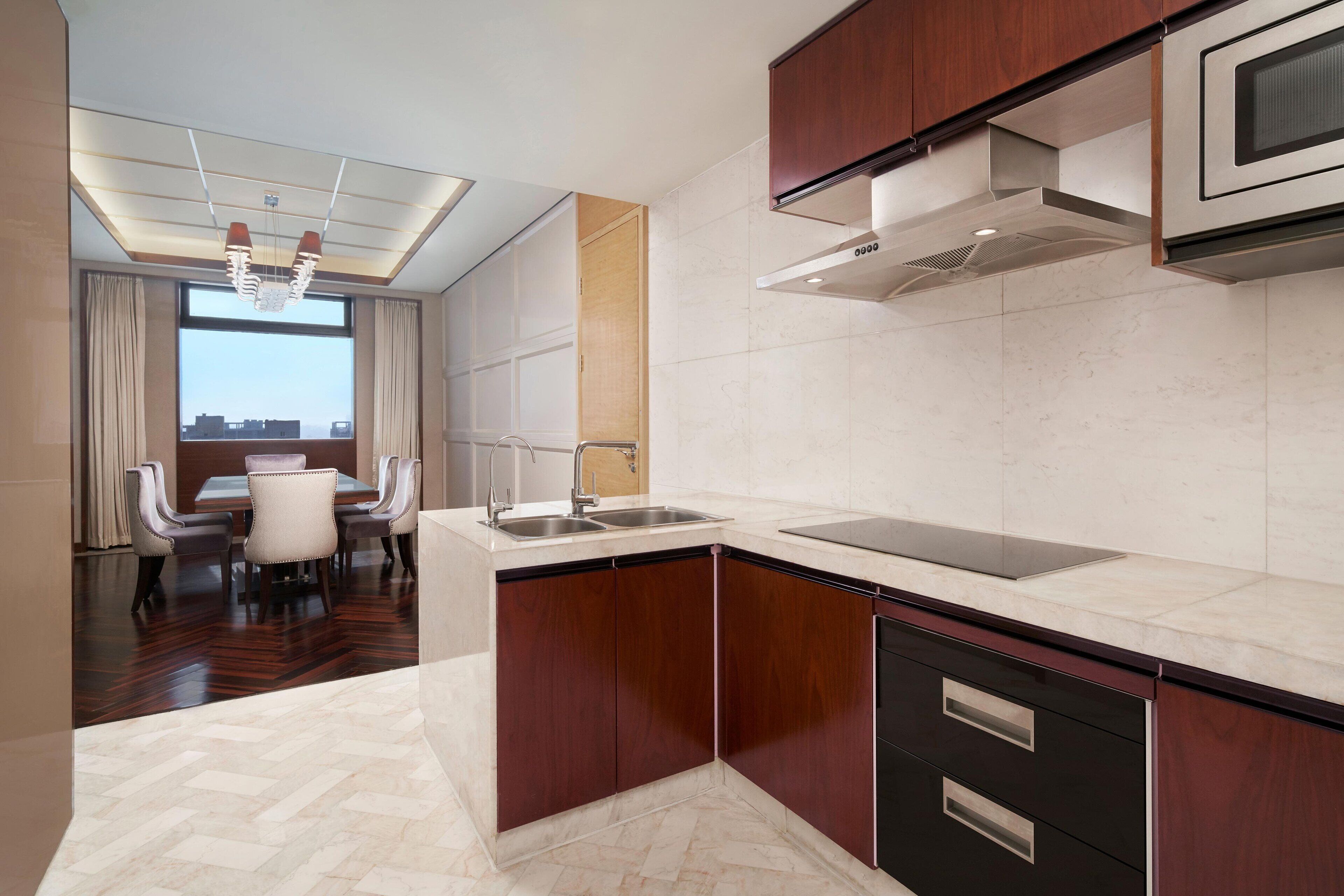 A modern kitchen with a built-in oven, a microwave, and a sink. There is a dining area with a table and chairs visible in the background.