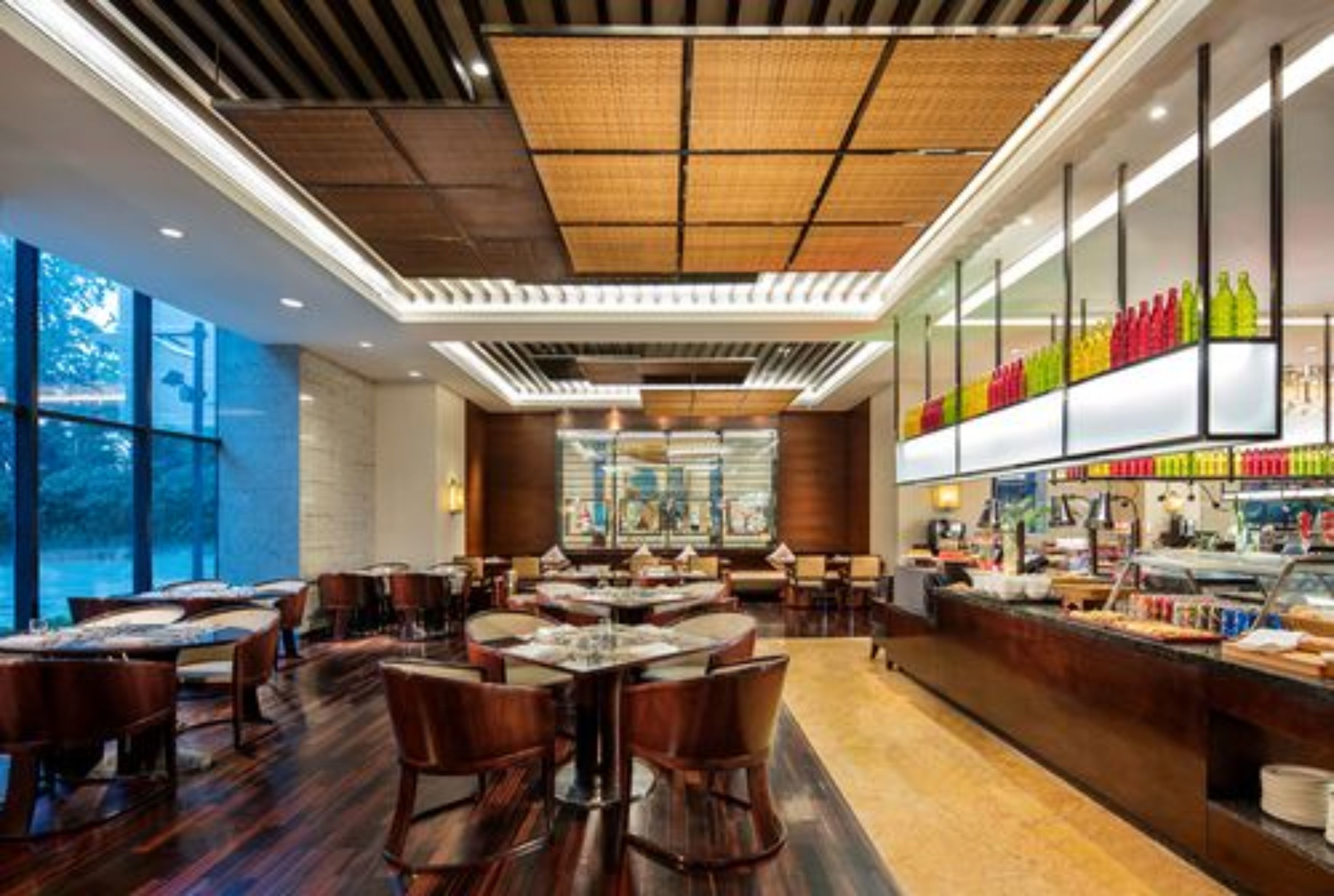 A restaurant with wooden tables and chairs, a bar area with colorful bottles, and large windows.