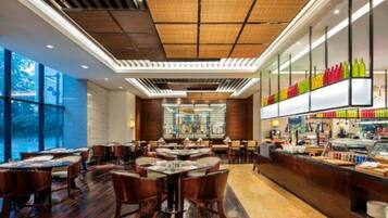 A restaurant with wooden tables and chairs, a bar area with colorful bottles, and large windows.