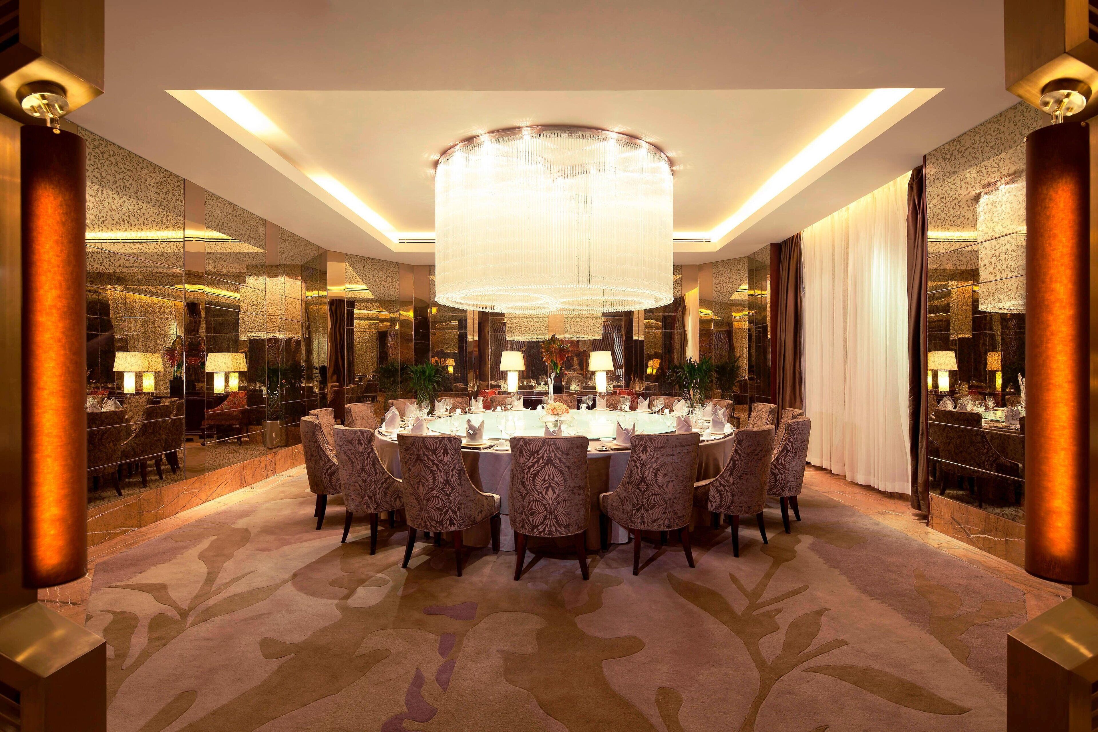 A formal dining room with a large chandelier, round table, and patterned chairs.