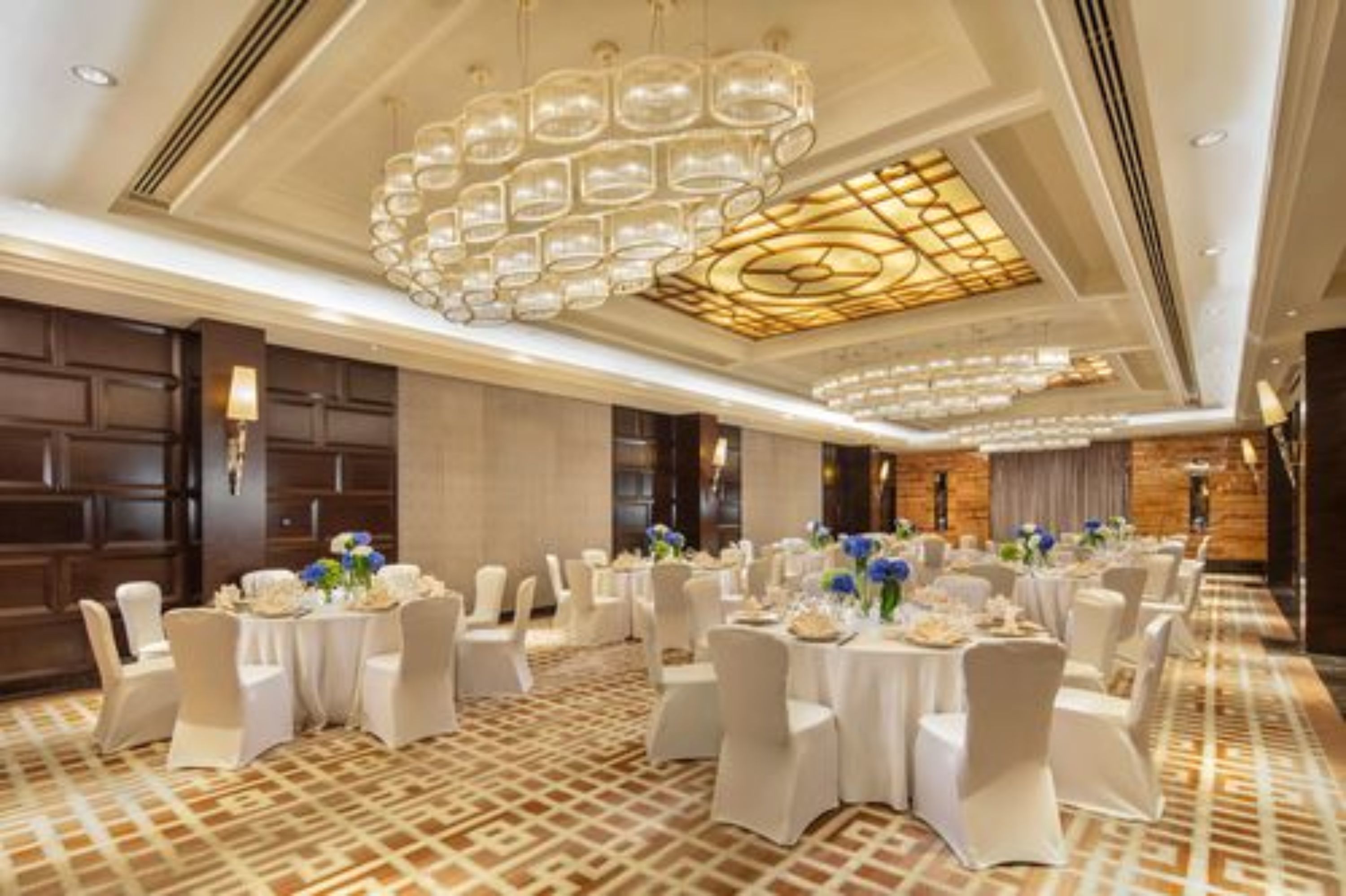 A banquet hall with round tables, white chairs, and a patterned carpet.