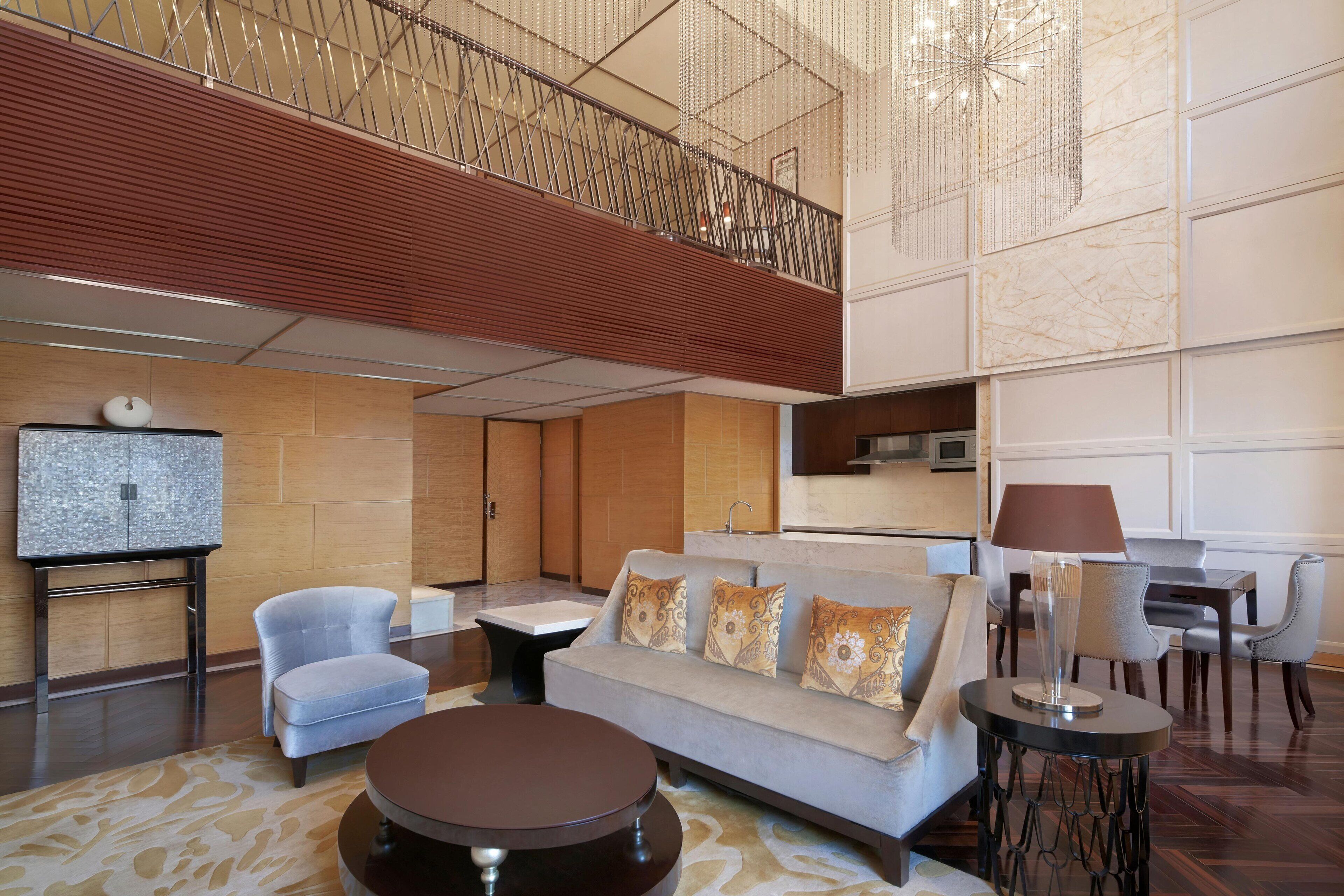 A spacious lobby with a high ceiling, a modern sofa, a round coffee table, and a dining area with chairs and a table.