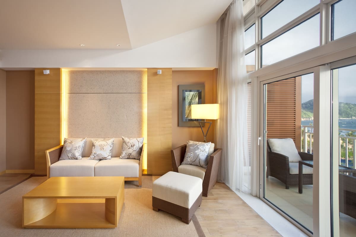 Una habitación de hotel moderna con sofá, reposapiés y una mesita de centro. Hay una ventana grande con vistas al exterior.
