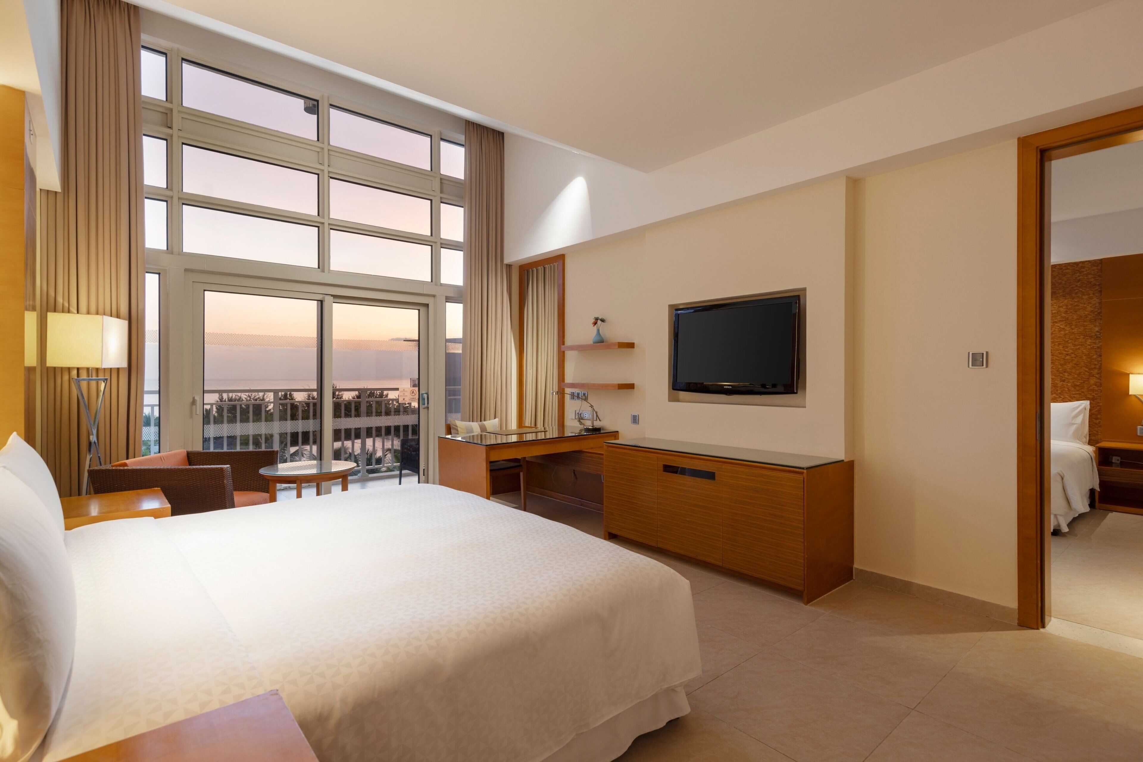 A hotel room with a large bed, a desk, a television, and a balcony with a view.