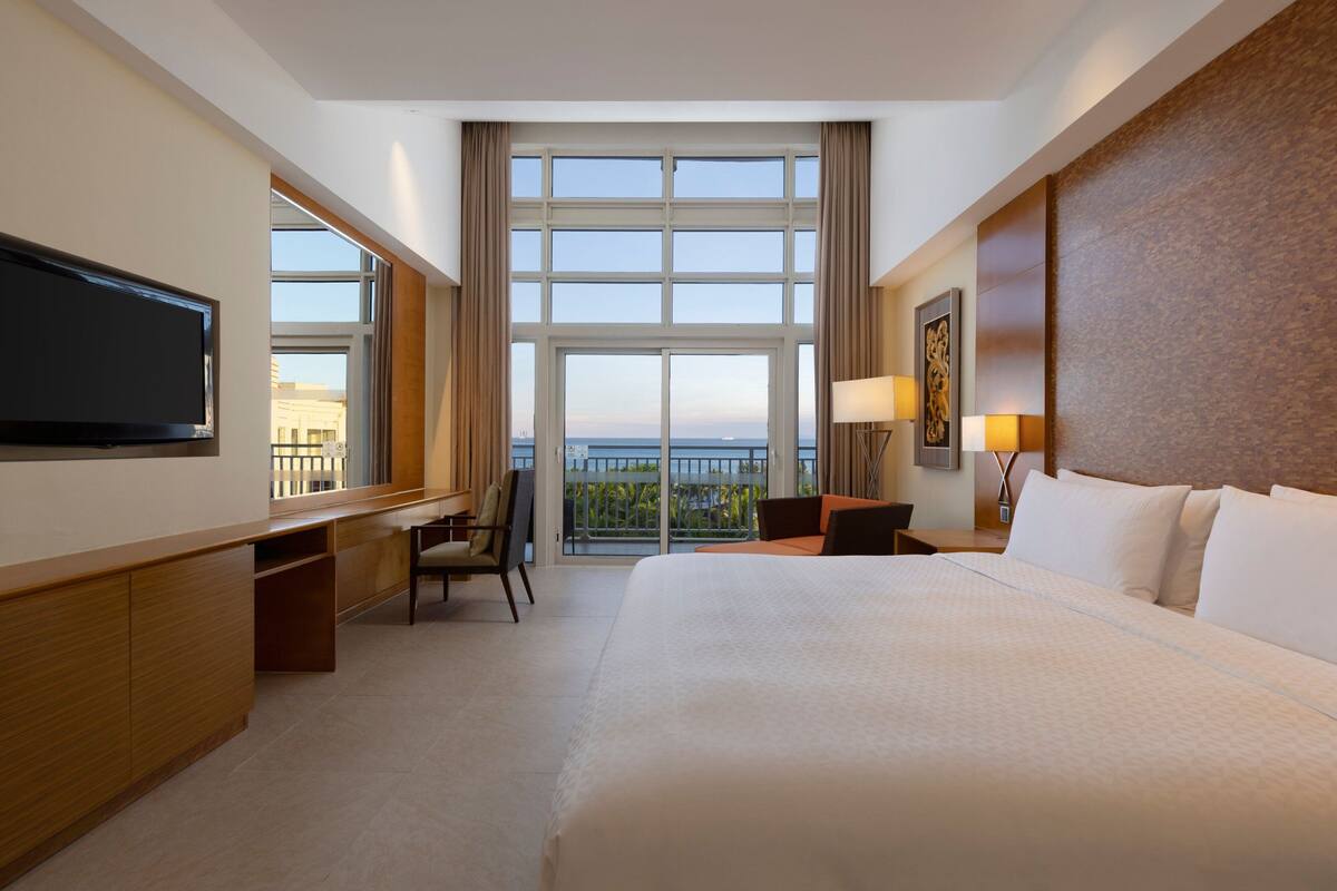 Una habitación de hotel con una cama grande, un escritorio, una silla, un televisor, una ventana con vistas y una lámpara.