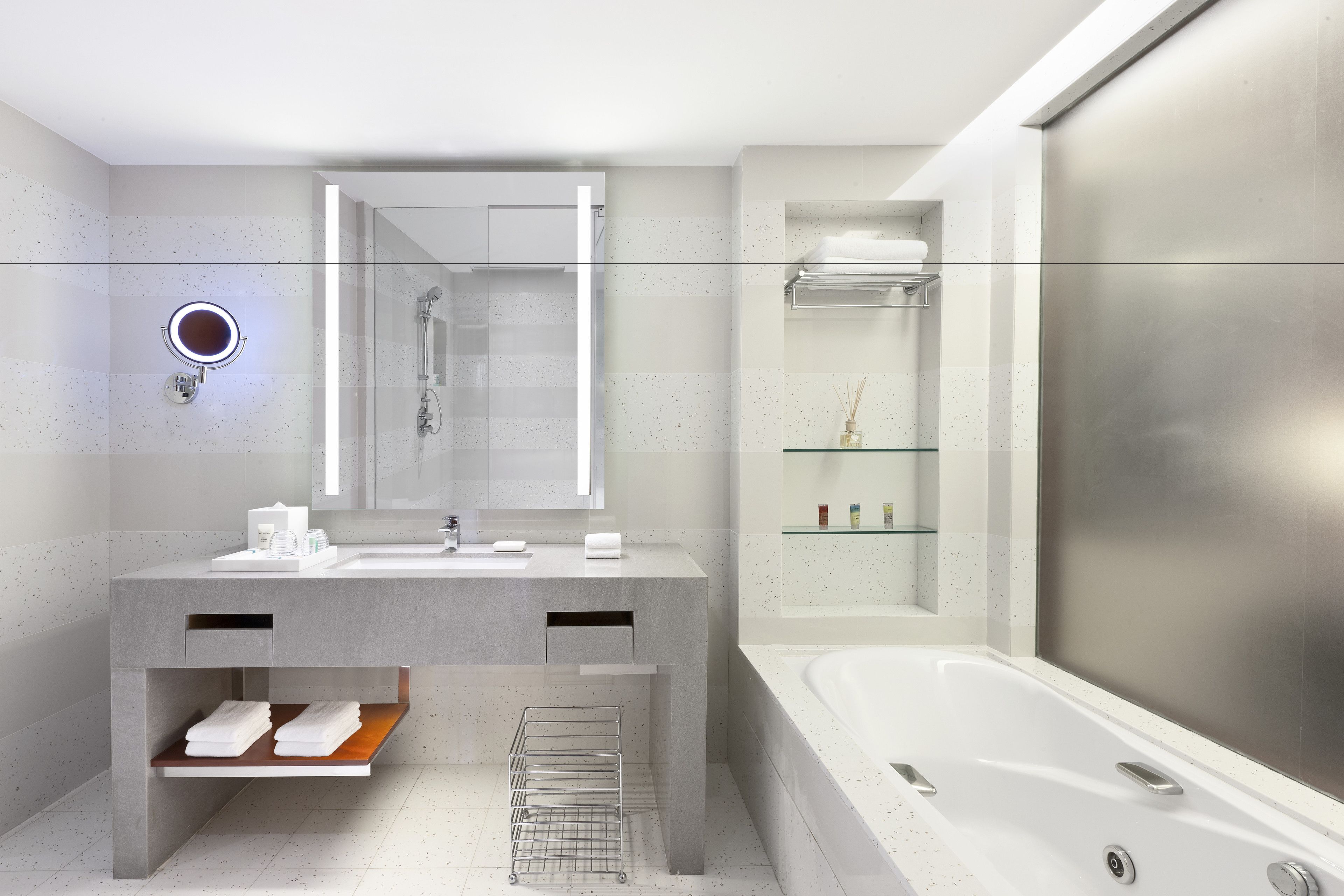 Un bany modern amb una banyera gran, un lavabo amb mirall i una estant amb productes de tocador.
