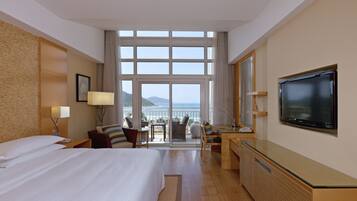 Habitación de hotel con una cama grande, un escritorio, un televisor y un balcón con vistas al mar.