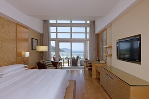Habitación de hotel con una cama grande, un escritorio, un televisor y un balcón con vistas al mar.