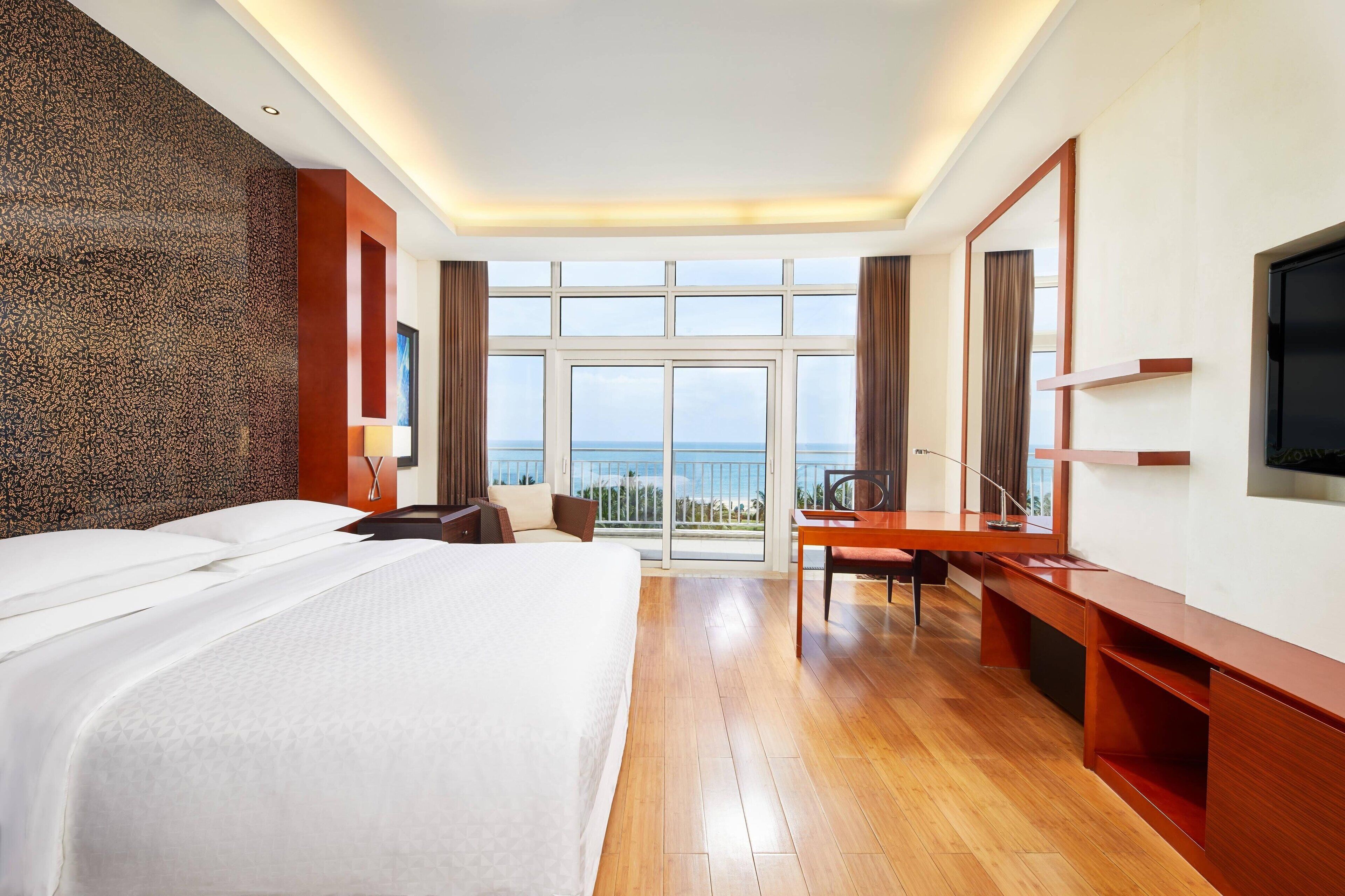 Una habitación de hotel con una cama grande, un escritorio, una silla, un televisor y un balcón con vistas al mar.