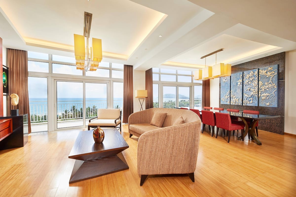 Amplia sala de estar con un gran ventanal, un sofá, una mesa de comedor con sillas y un elemento decorativo en la pared.
