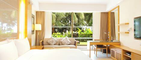 Una habitación de hotel moderna con una cama grande, un escritorio y un televisor. Tiene un balcón con vistas a zonas verdes.