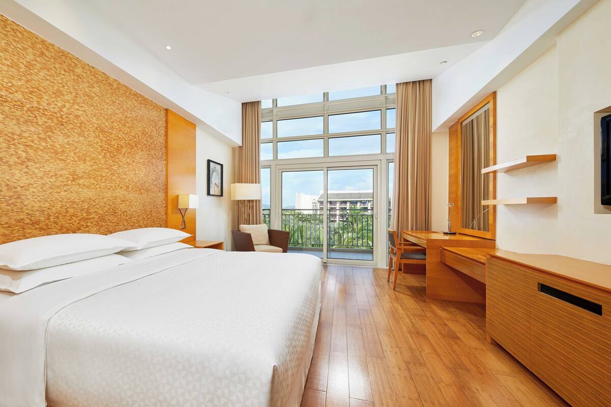 Una habitación de hotel con una cama grande, un escritorio, una silla y un balcón con vistas.