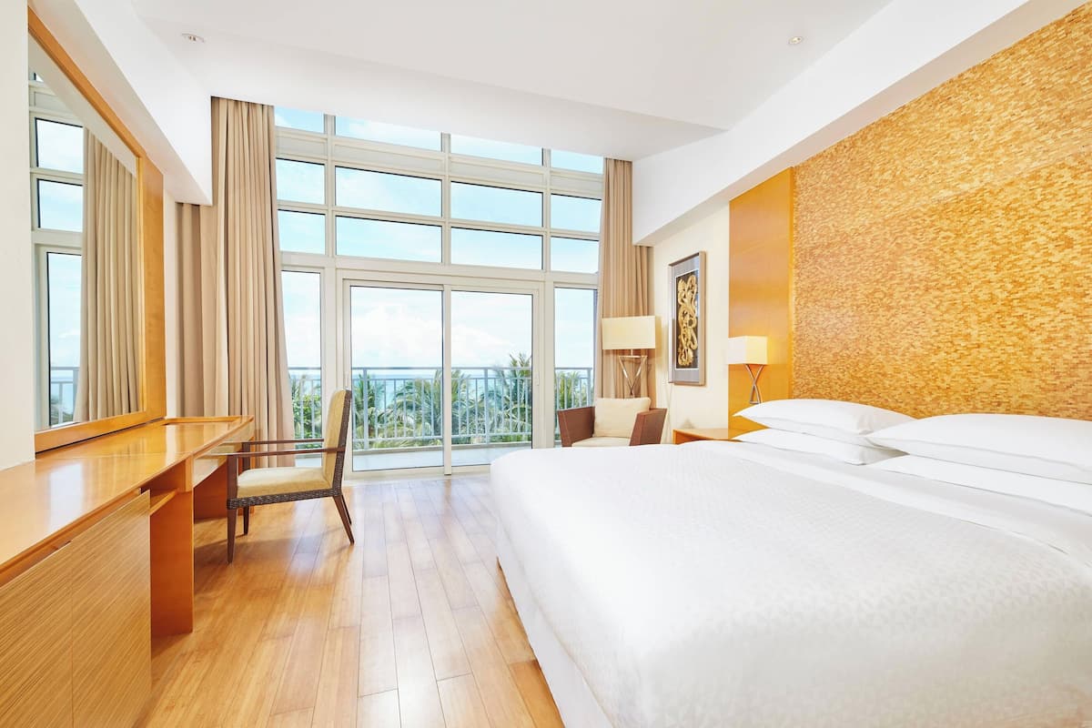Habitación de hotel con una cama grande, un escritorio, una silla, un balcón con vistas y una pared con textura.