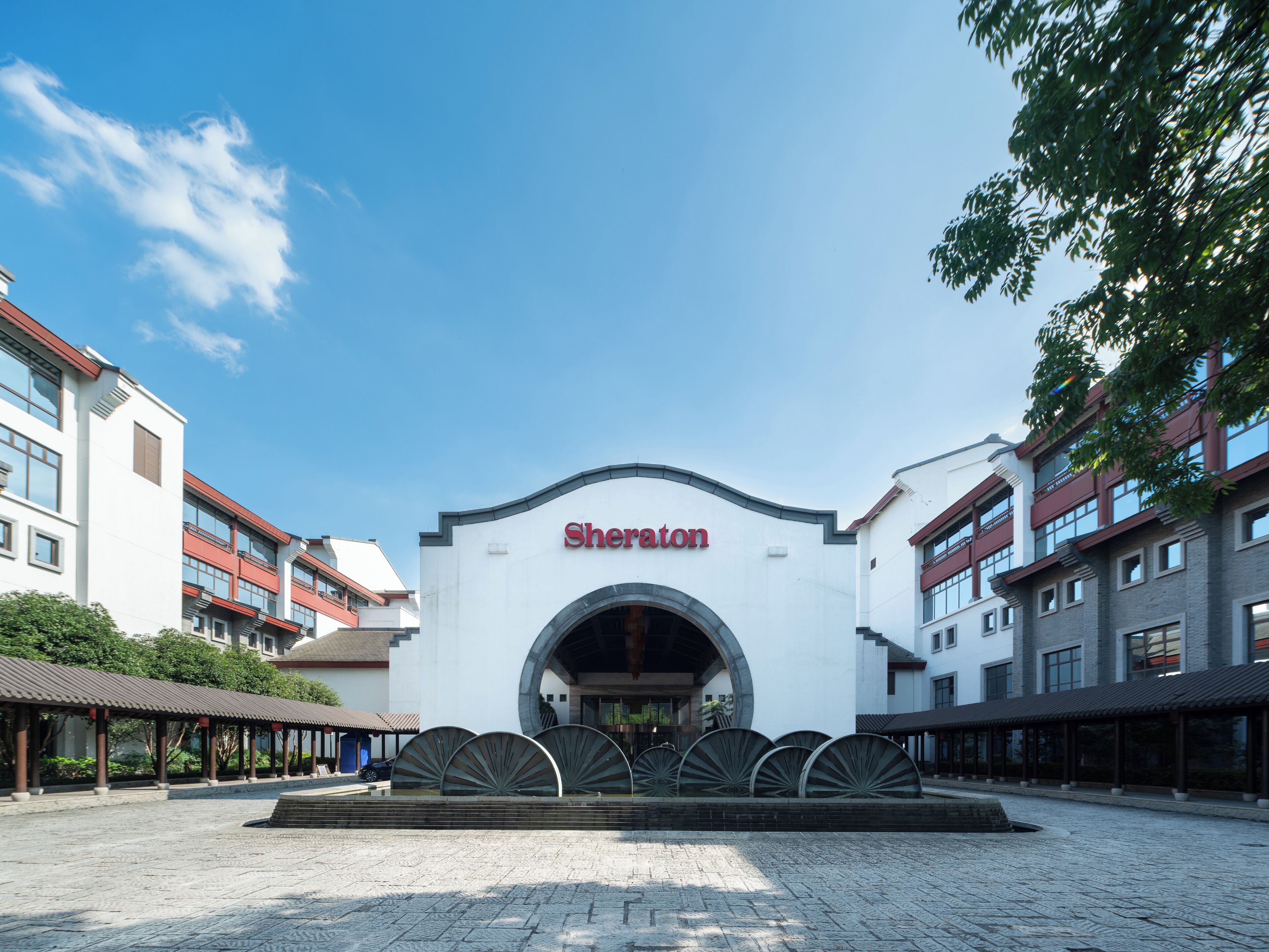 A Sheraton hotel entrance with a modern design, featuring a large arched entrance and a courtyard with a fountain.