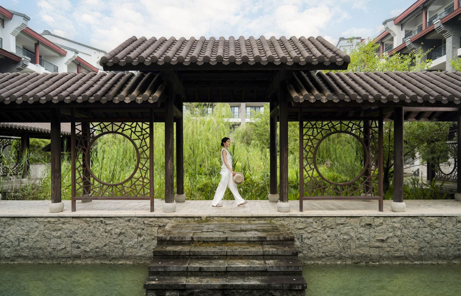 A traditional pavilion with a stone base and a tiled roof, overlooking a body of water.