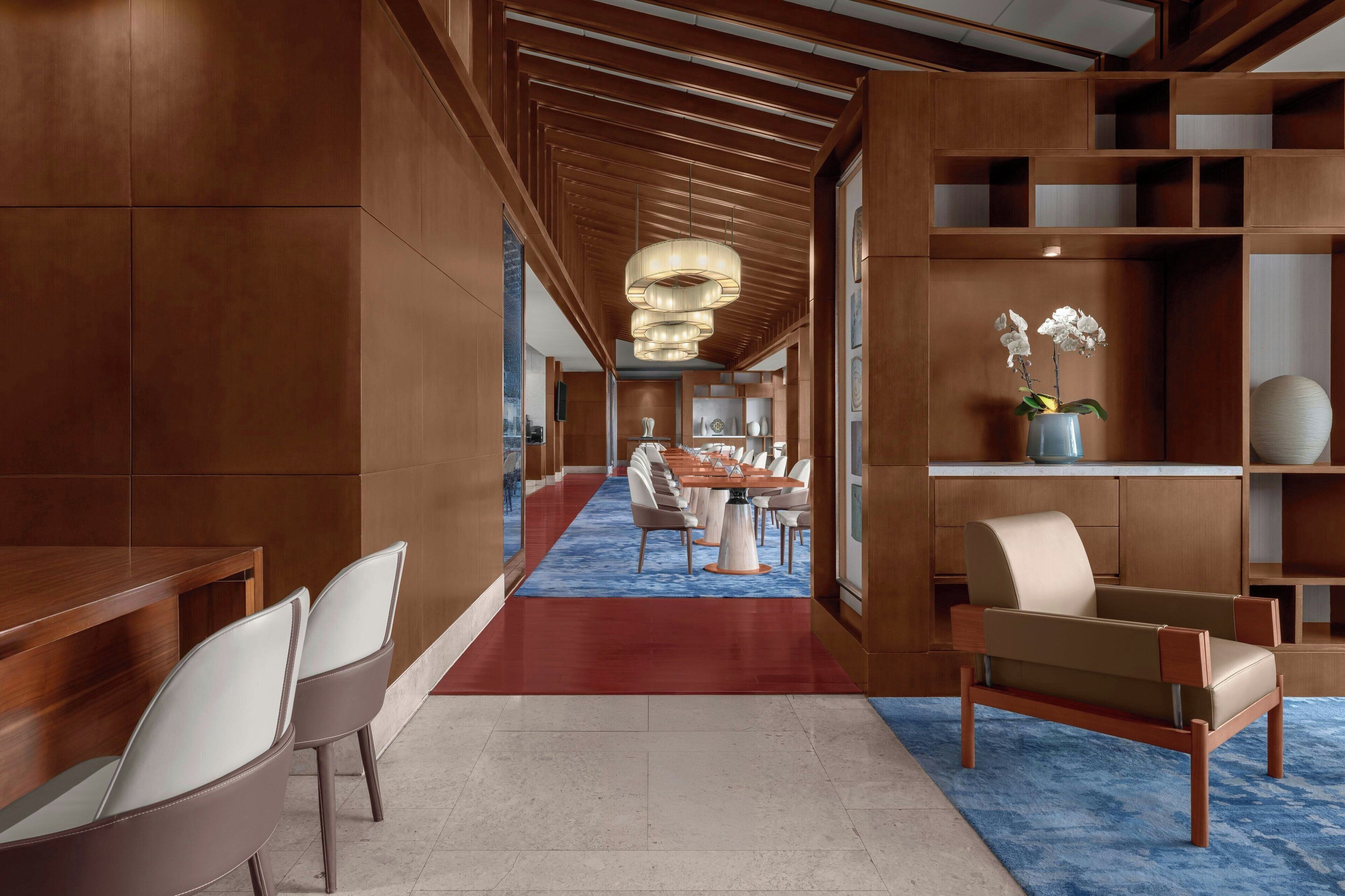 Un hall d’hôtel moderne avec un long comptoir d’accueil, un espace salon et un coin repas comprenant une longue table et des chaises.