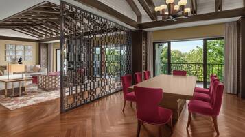 A spacious dining area with a large wooden table and matching chairs, a decorative partition, and a view of greenery through large windows.