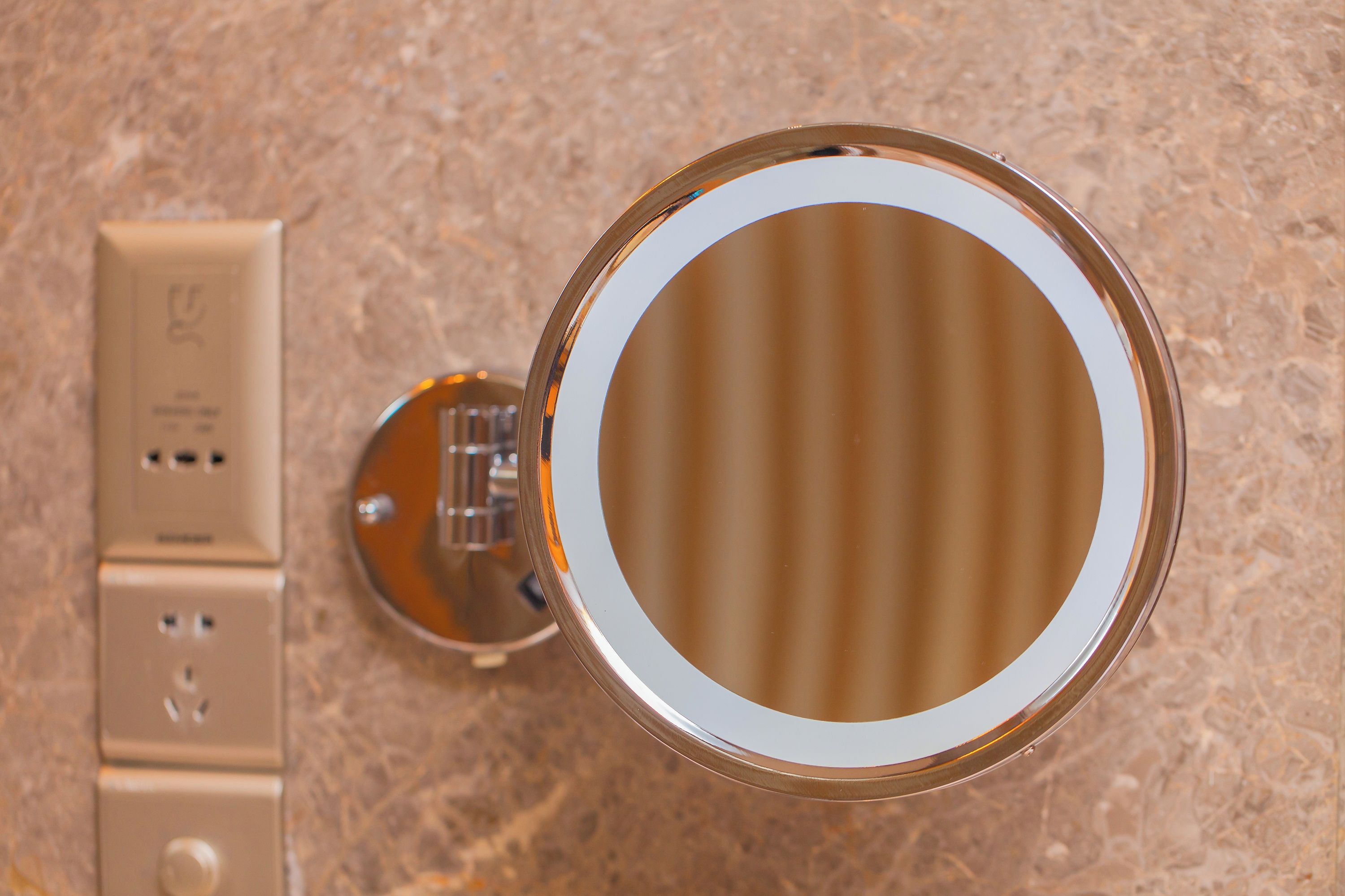 A bathroom with a round mirror, a wall-mounted light, and a power outlet.