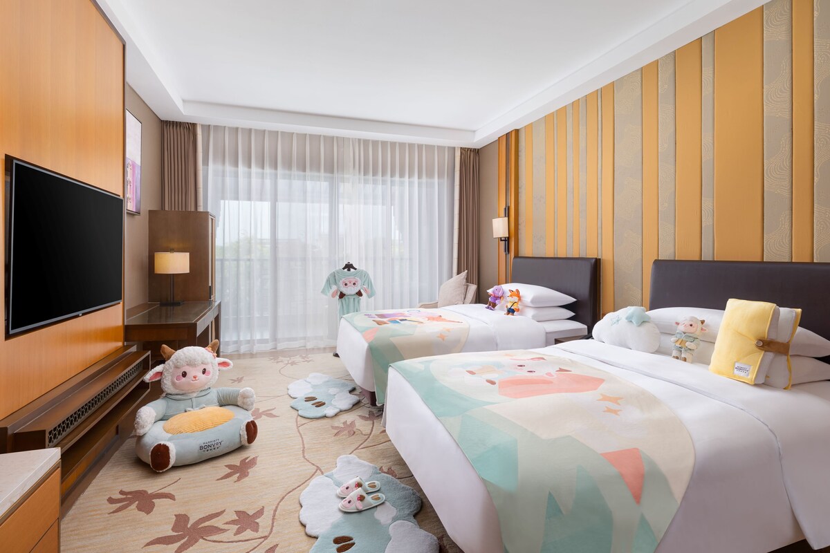 A hotel room with two beds, a TV, a sofa, and a large window with curtains.
