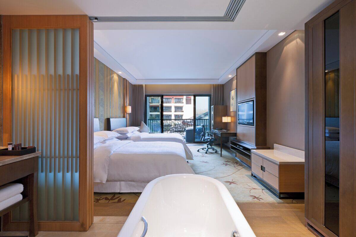 A hotel room with two beds, a bathtub, a desk, and a TV.