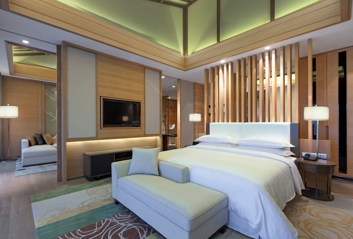 A modern hotel room with a large bed, a TV, a sofa, and a desk.