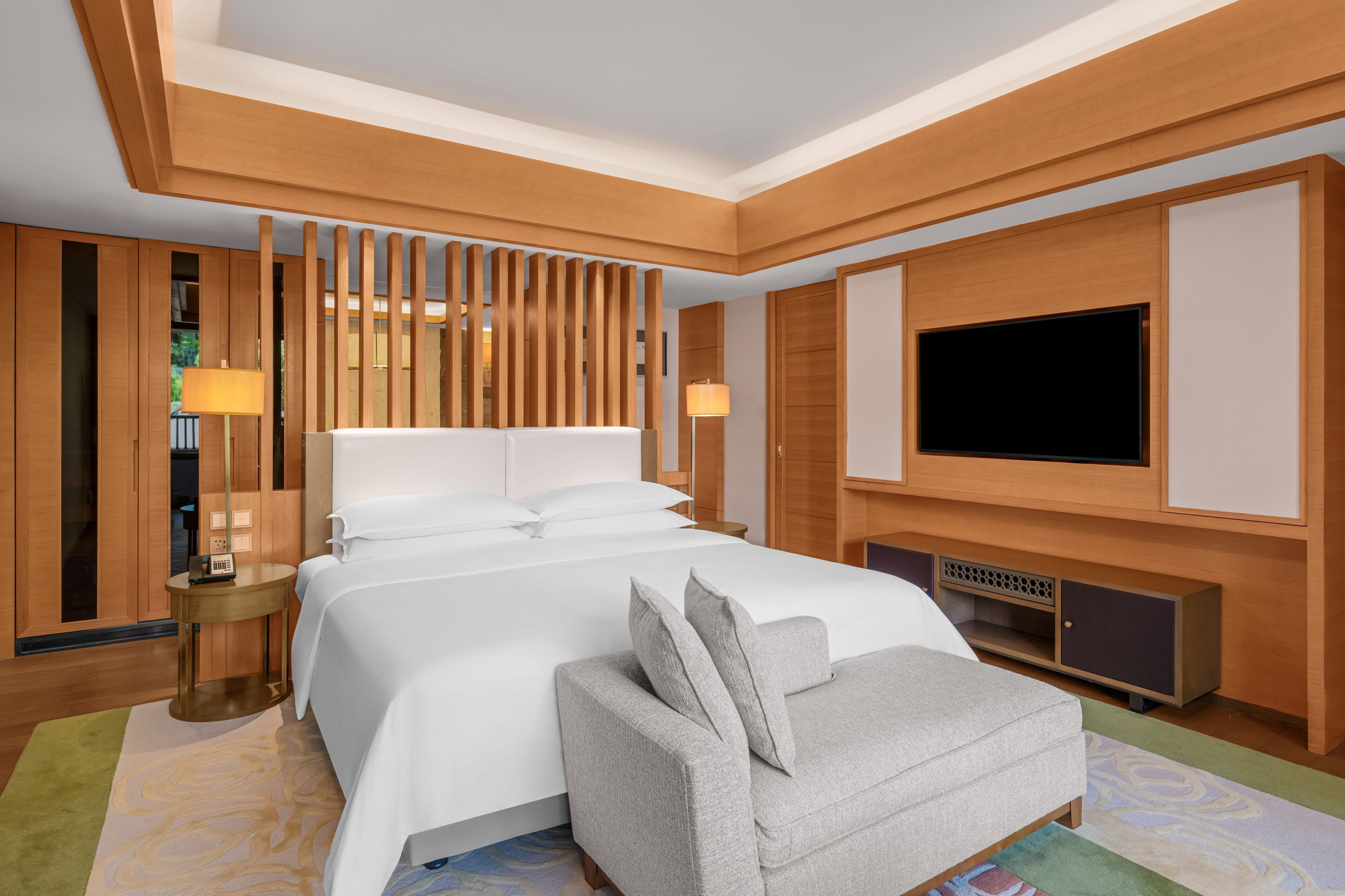 Une chambre d’hôtel avec un grand lit, une télévision, un canapé et un mur recouvert de panneaux de bois.