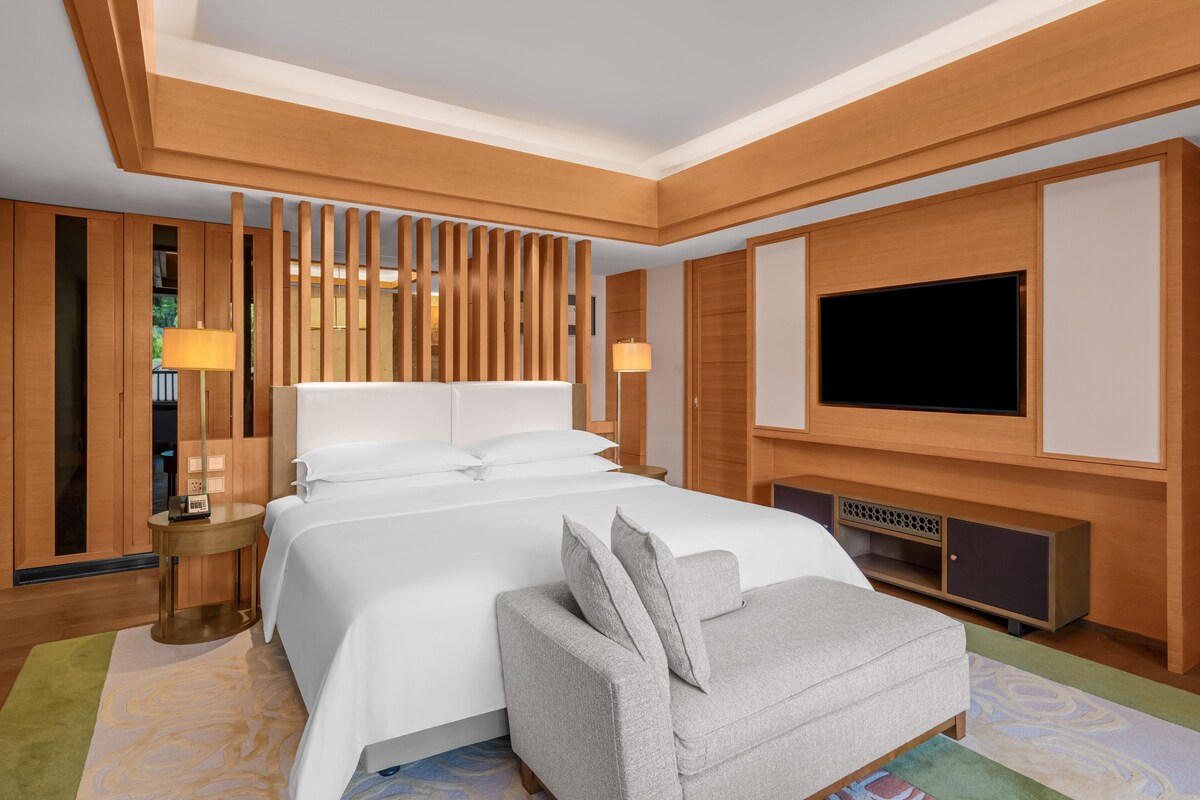 A hotel room with a large bed, a TV, a sofa, and a wooden panel wall.