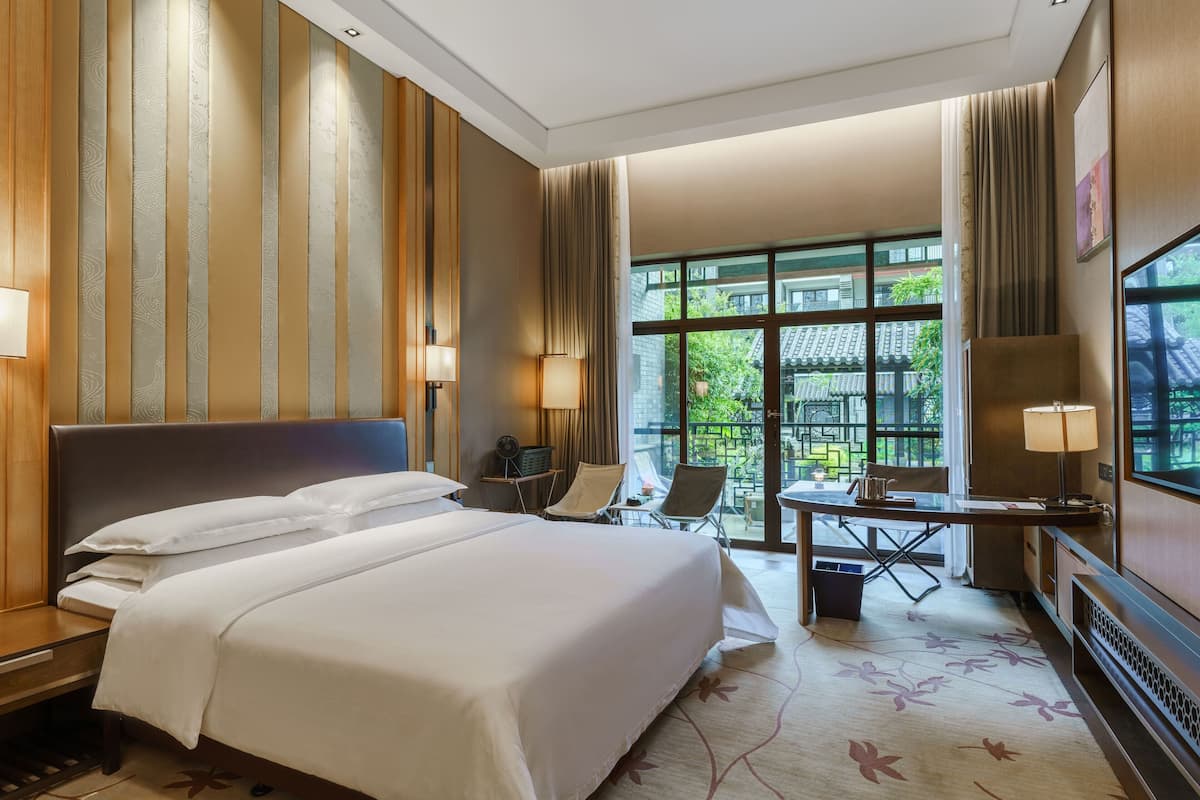 A hotel room with a large bed, a desk with a chair, a TV, and a view of the outside.