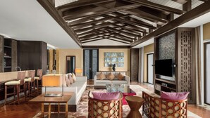 A spacious living area with a high ceiling, wooden beams, a sofa set, a coffee table, two side tables with patterned cushions, a flat-screen TV, and a decorative wall panel. - Sheraton Grand Hangzhou Wetland Park Resort (Hangzhou)