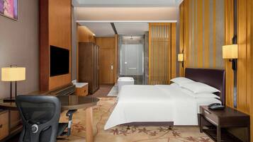 A hotel room with a bed, desk, chair, TV, and a bathroom with a shower and toilet.