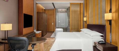 A hotel room with a bed, desk, chair, TV, and a bathroom with a shower and toilet.