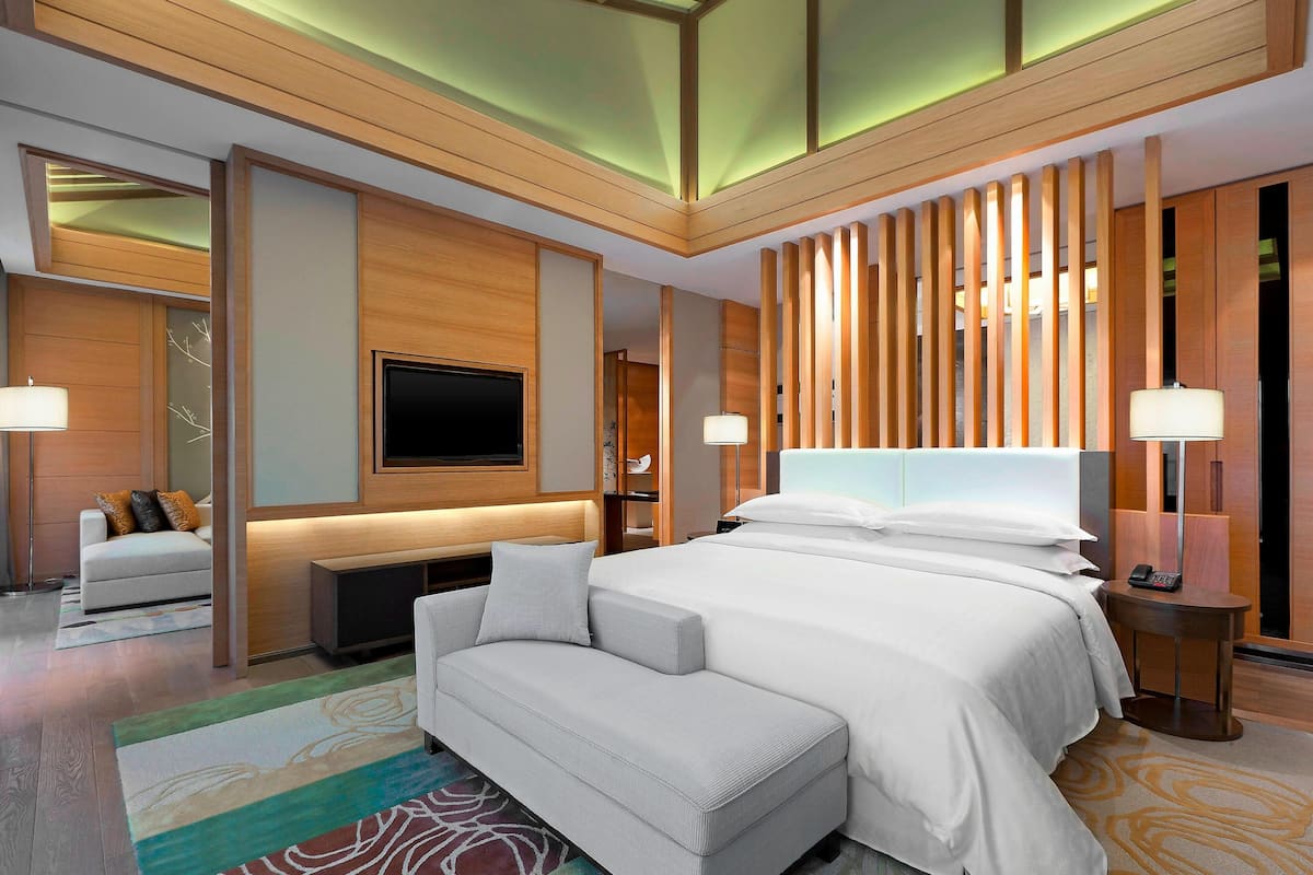 A modern hotel room with a large bed, a flat-screen TV, a sofa, and a desk.