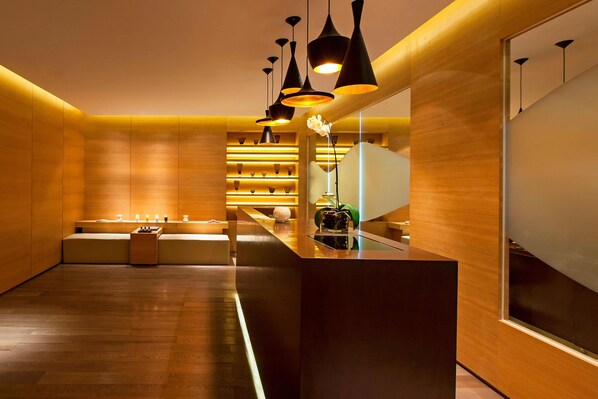 Un moderno vestíbulo de hotel con un mostrador de recepción de madera, lámparas colgantes negras y una zona de estar con una planta.