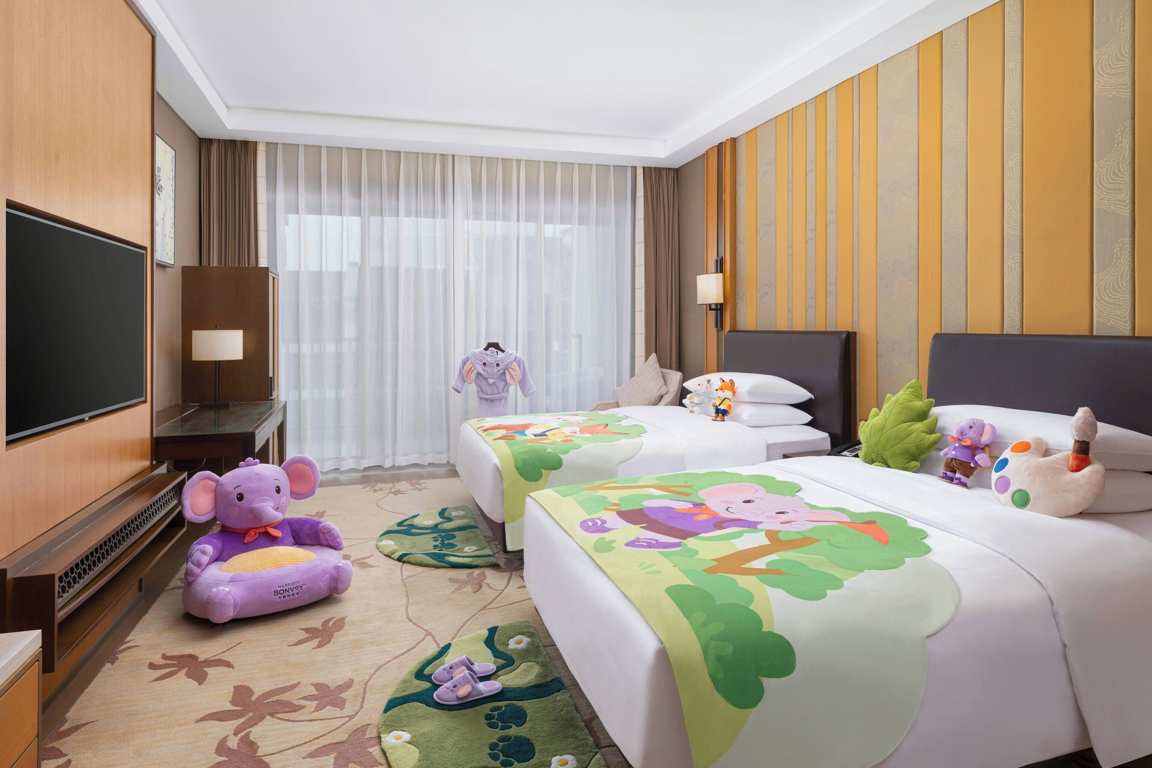 Une chambre d’hôtel avec deux lits, une télévision, un jouet en peluche et un tapis décoratif.