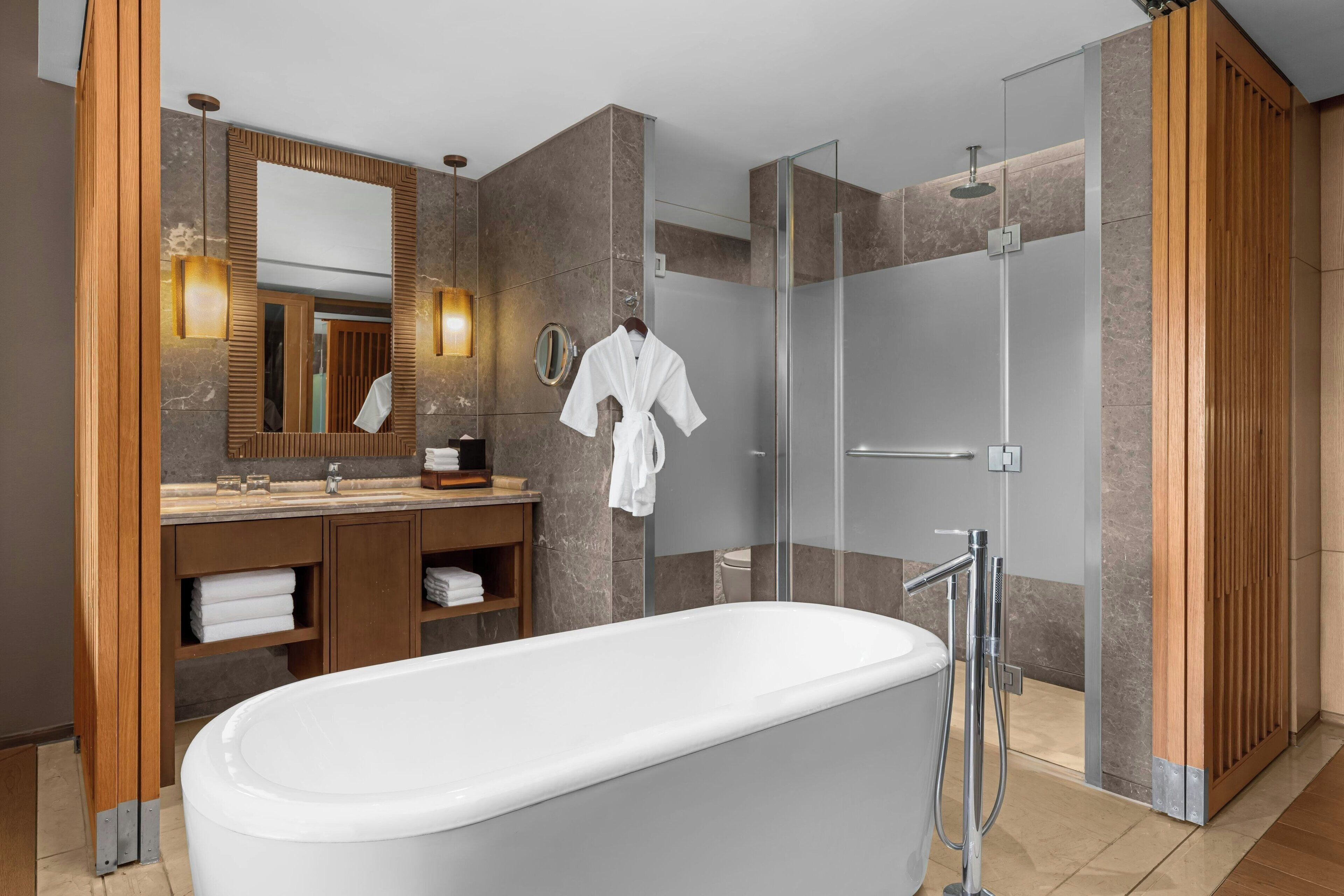 Un baño moderno con una bañera independiente, una ducha con cerramiento de vidrio y un tocador con espejo y toallero.