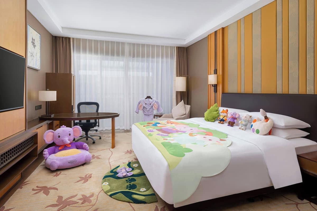 A hotel room with a bed, a desk, a chair, a television, and a window with curtains.