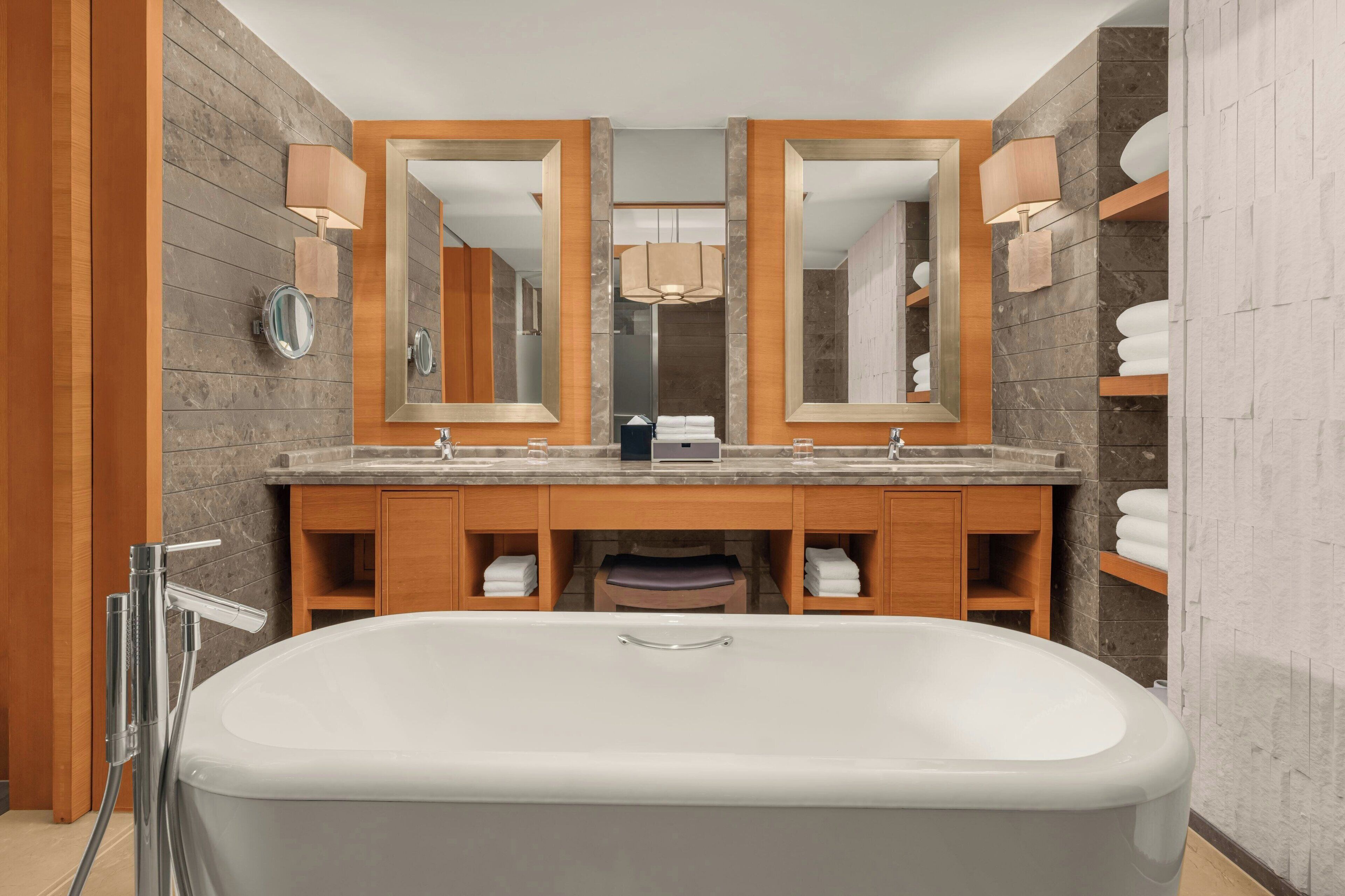 Un baño moderno con una bañera grande, lavamanos dobles, tocador de madera y dos espejos amplios.