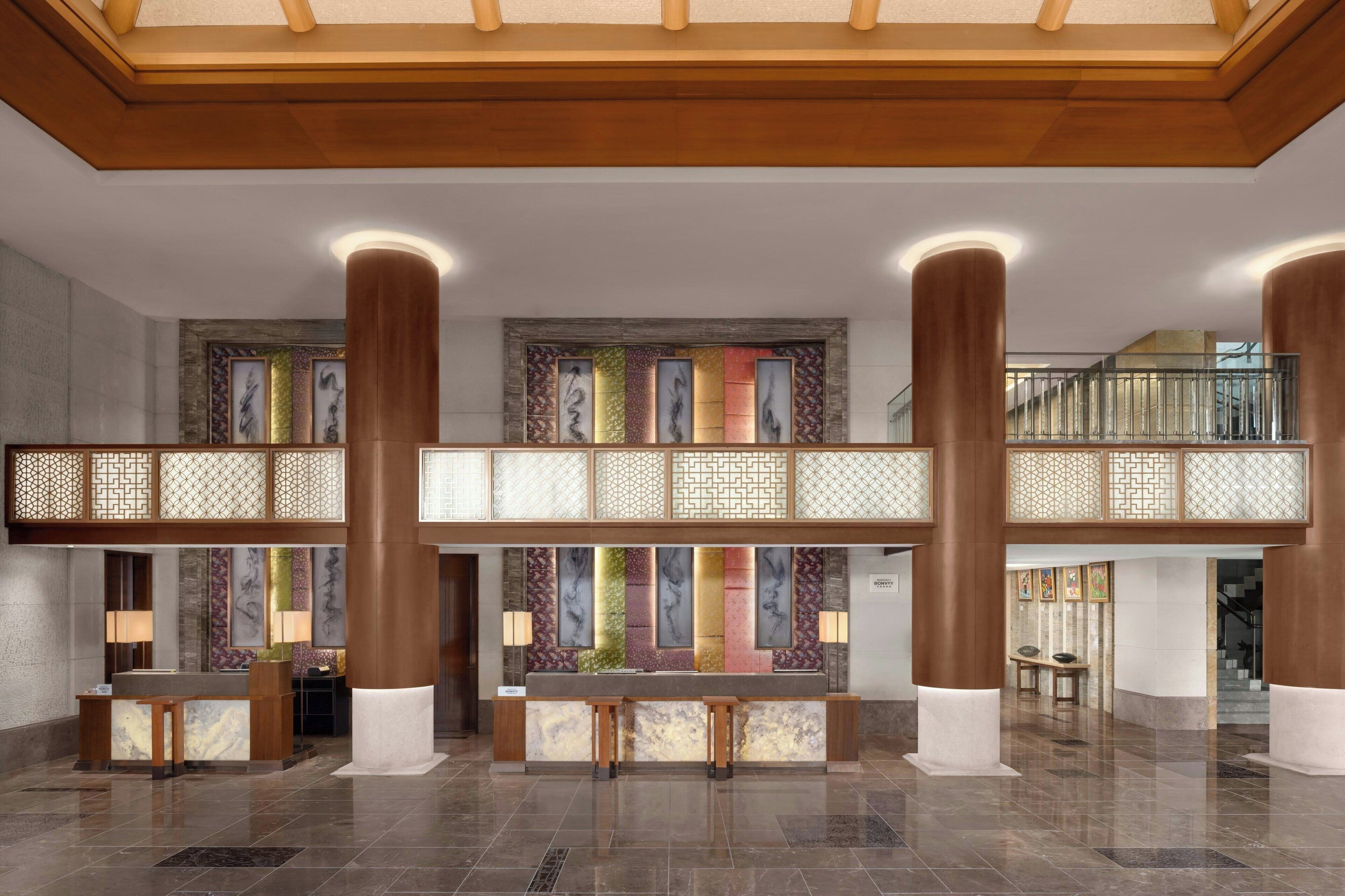 A spacious lobby with a reception desk, two seating areas, and a staircase leading to an upper level.