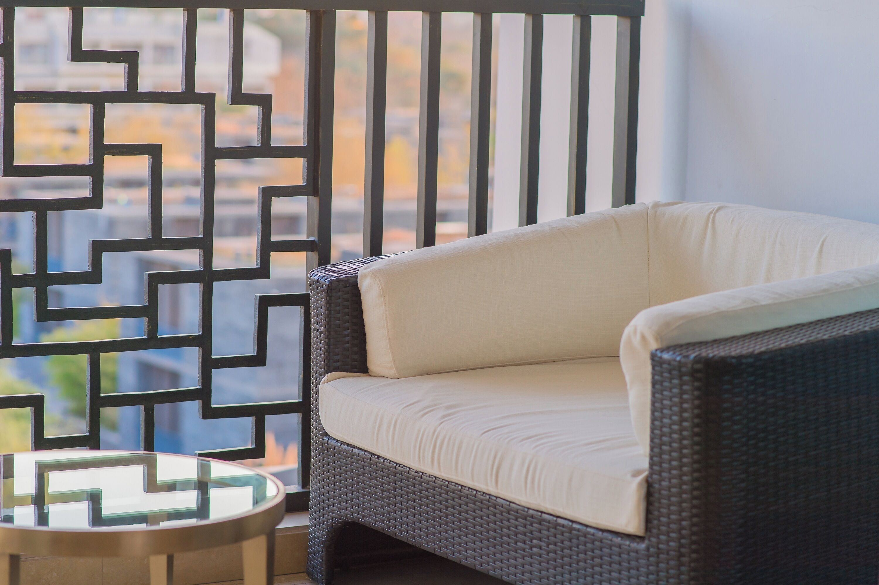 A wicker sofa with a light cushion, a round glass table, and a geometric metal partition.