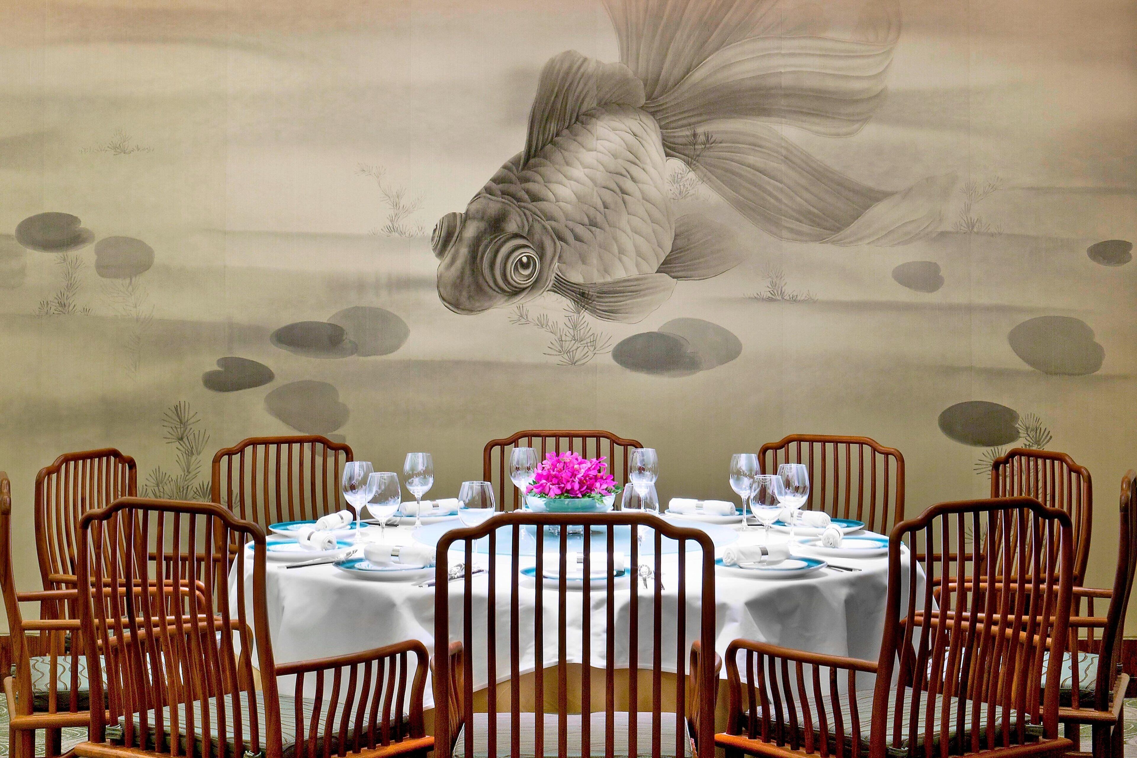 A dining area with a table set for four, surrounded by wooden chairs, and a large fish mural on the wall.