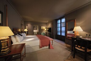 Habitación de hotel con una cama grande, mesitas de noche, un escritorio y una silla. Se aprecia una ventana con vistas al exterior.