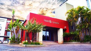 Um hotel com fachada vermelha, palmeiras e um edifício de tijolos ao fundo.