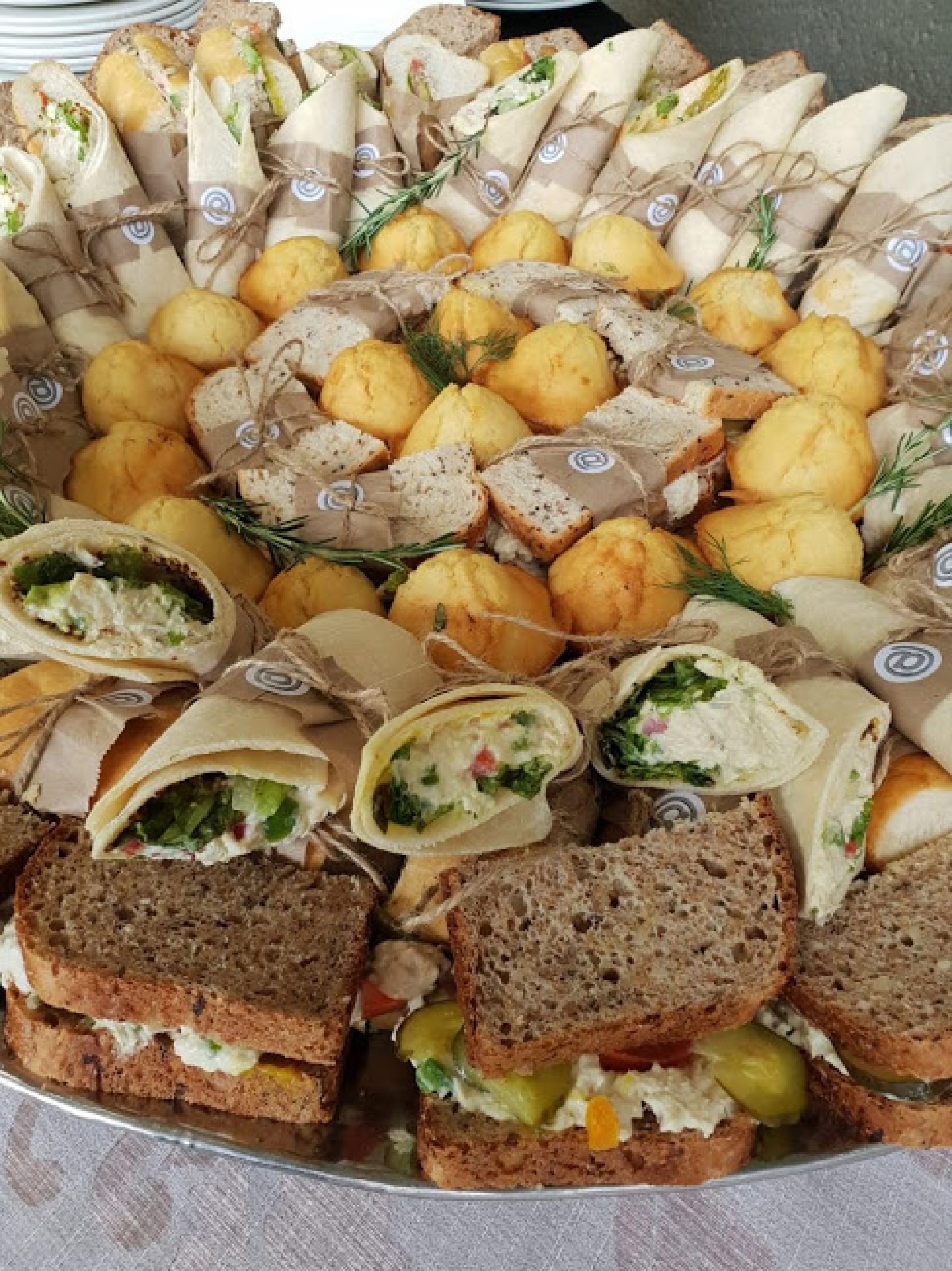 A platter of assorted sandwiches and snacks, including wraps and bread rolls, arranged on a table.
