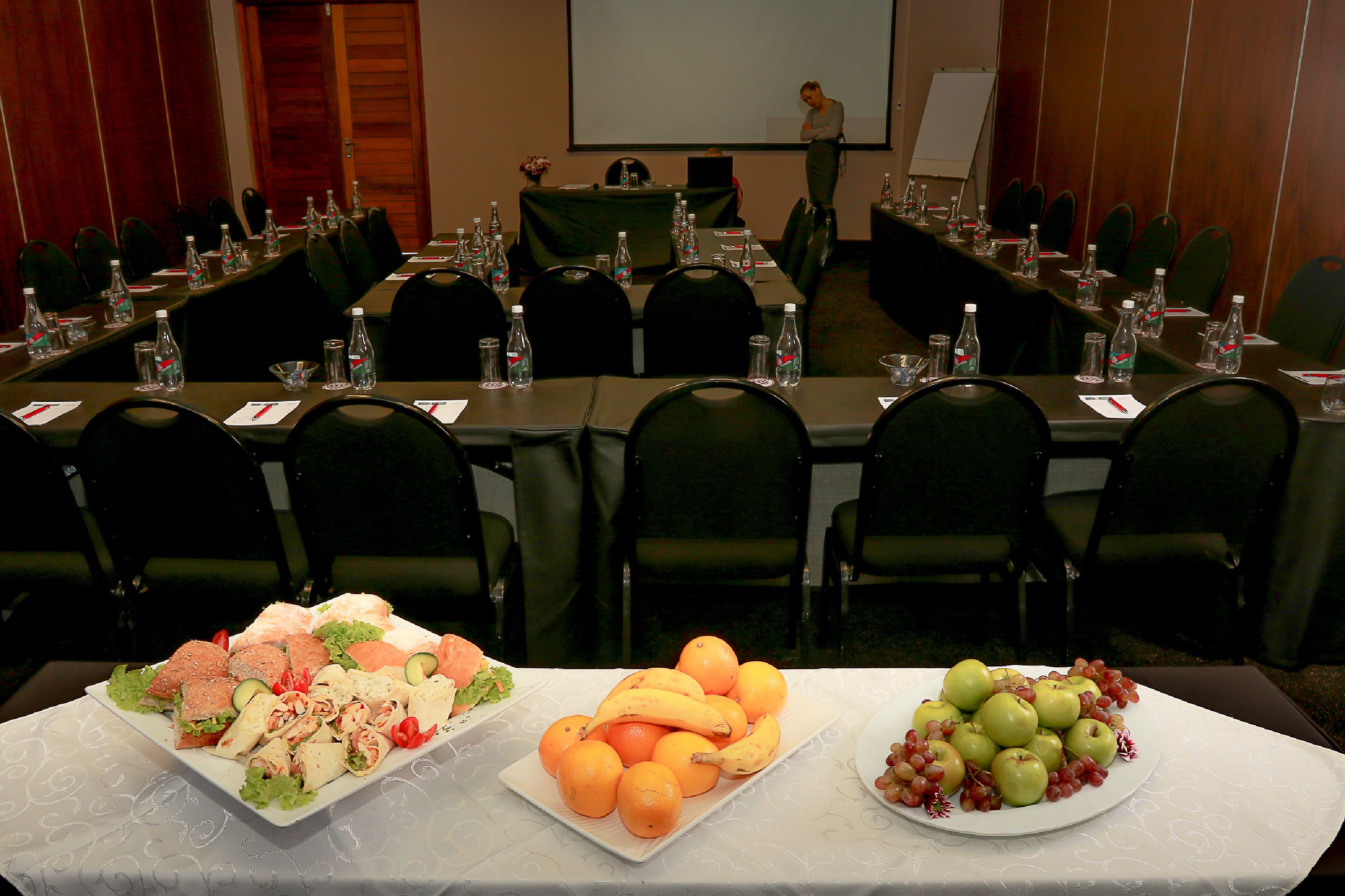 A conference room with multiple tables, chairs, and a presentation screen.