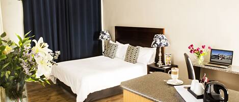 A hotel room with a large bed, a desk with a laptop, a coffee maker, and a vase with flowers.