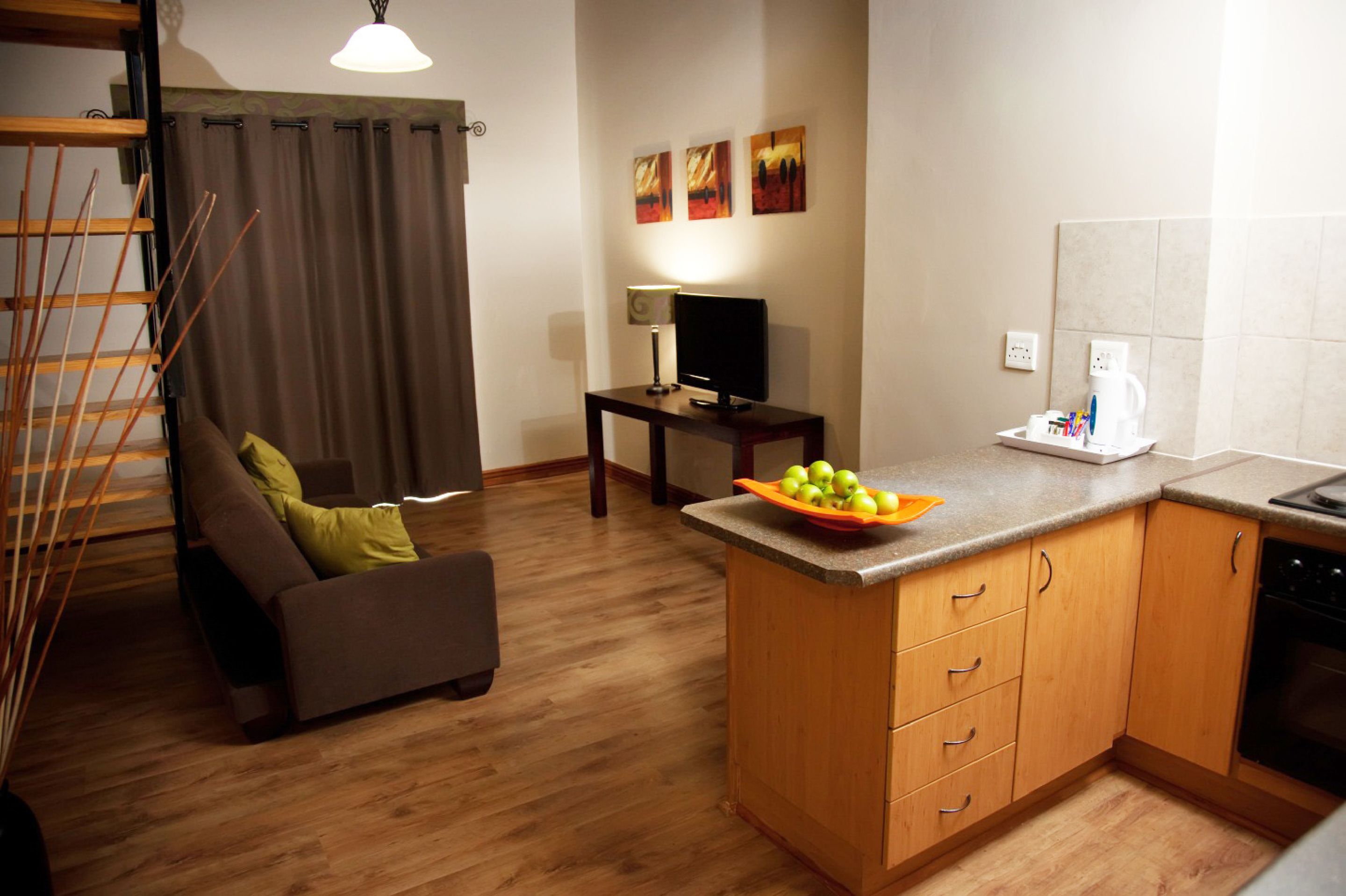 Una cocina moderna con armarios de madera, un área de comedor con un sofá, un televisor y un frutero en la encimera.
